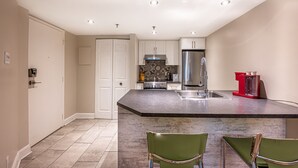 Een moderne keuken met witte kasten, een roestvrijstalen koelkast en een marmeren eiland met twee groene stoelen.
