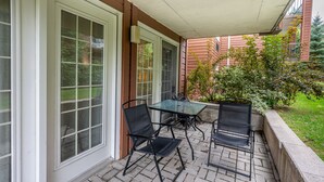 Overdekt terras met glazen tafel en vier stoelen, omgeven door een bakstenen muur en een kleine tuin.