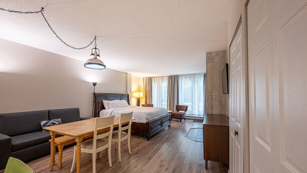 A hotel room with a bed, a desk, a chair, a sofa, and a dining table.