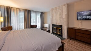 A hotel room with a large bed, a fireplace, a TV mounted on the wall, and a desk with a chair.