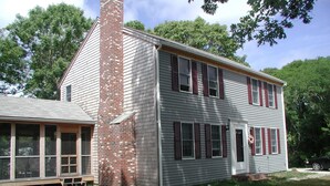 A two-story house with a brick chimney, large windows, and a porch.