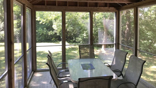 A covered patio with a table and chairs, large windows, and a ceiling fan.