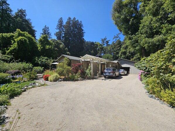 A house with a gravel driveway, parked cars, and a garden with various plants and flowers.
