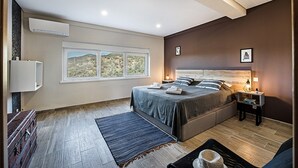 A modern bedroom with a large bed, a window with a view, a bedside table with a lamp, and a small rug.