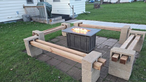 An outdoor fire pit with a stone table and benches, surrounded by a grassy area and a paved walkway. - Family, Group Friendly, Large Yard, Only 6 Miles To Duluth, MN!  EV Charger (Superior)