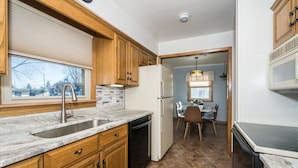 A compact kitchen with wooden cabinets, a built-in dishwasher, and a window overlooking a residential area. - Family, Group Friendly, Large Yard, Only 6 Miles To Duluth, MN!  EV Charger (Superior)