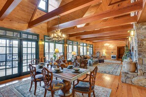 A spacious dining area with a wooden table and chairs, a chandelier, and large windows allowing natural light. - Lakefront Custom-Built Mentone Home: Game Room! (Mentone)