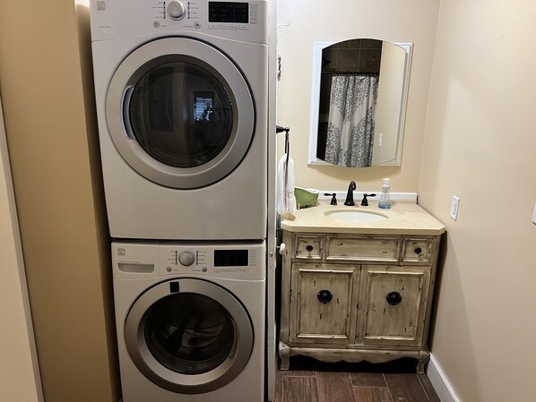 A compact laundry area with a stacked washer and dryer, a vintage-style vanity with a mirror, and a sink. - Get to BLUES-in' at Rusty's Roost, adjacent to downtown Clarksdale, MS (Clarksdale)