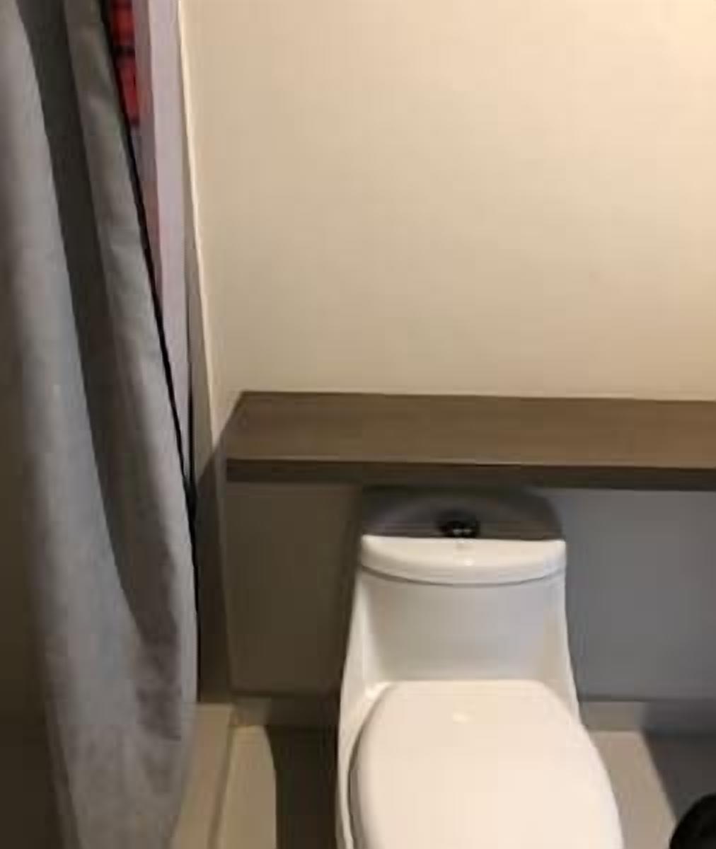 Un inodoro en un baño con una cortina gris que lo cubre parcialmente.