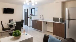 Eine moderne Küche mit Mikrowelle, Kühlschrank und Spüle. Es gibt eine Essecke mit Tisch und Stühlen sowie ein Wohnzimmer mit Sofa und Pflanze.