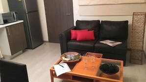 Ein Wohnzimmer mit einer schwarzen Ledersofa, einem kleinen Holztisch und einer Küchenzeile inklusive Kühlschrank und Mikrowelle.