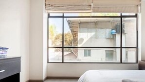 Ein Schlafzimmer mit großem Fenster, einem Bett und einer Kommode.