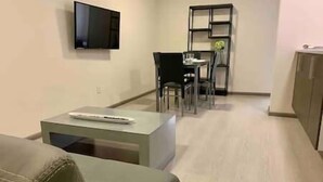 Ein Wohnzimmer mit einer Couch, einem Couchtisch, einem an der Wand montierten Fernseher und einem Essbereich mit Stühlen und Tisch.