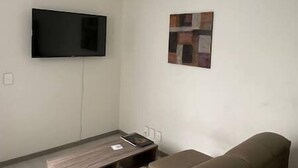 Un salon avec un téléviseur à écran plat fixé au mur, une petite table sur laquelle repose un livre et un canapé marron.
