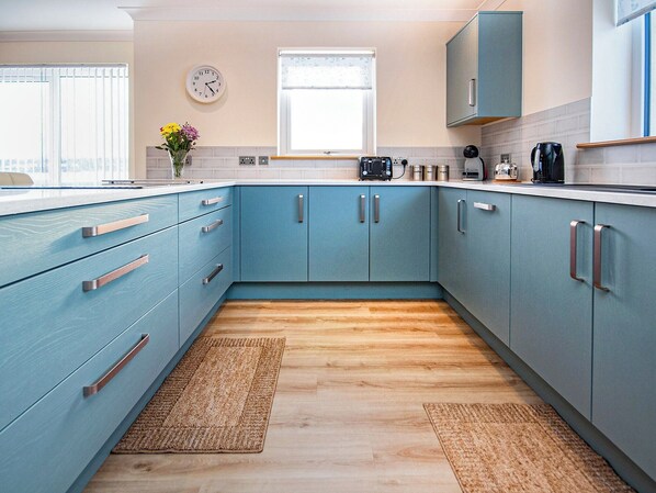 Una cocina moderna con gabinetes color turquesa, piso de madera y un reloj en la pared.