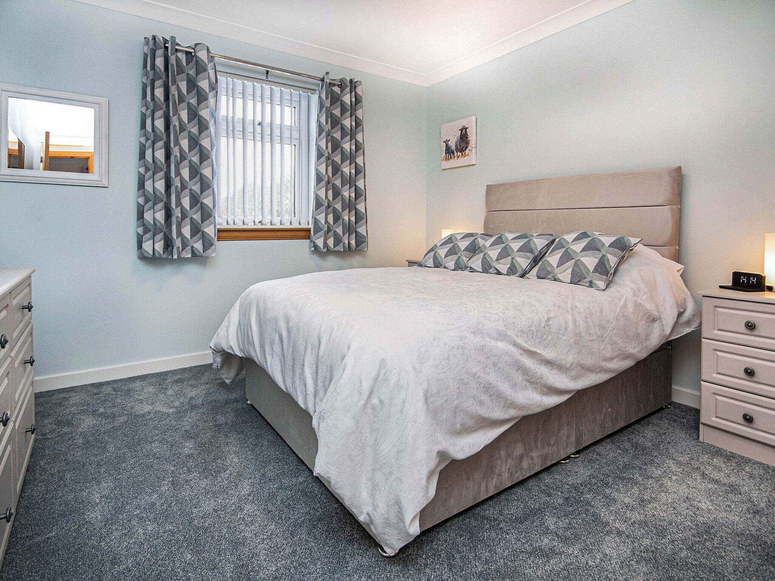 A bedroom with a bed, a nightstand, a dresser, a window with curtains, and a wall-mounted picture.