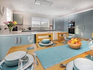 Una cocina moderna con armarios grises, una mesa de comedor puesta con platos, vasos y un cuenco de fruta.