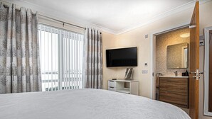 Ein Hotelzimmer mit einem großen Bett, einem an der Wand befestigten Fernseher, einem Schreibtisch mit Stuhl und einem Holzschrank.
