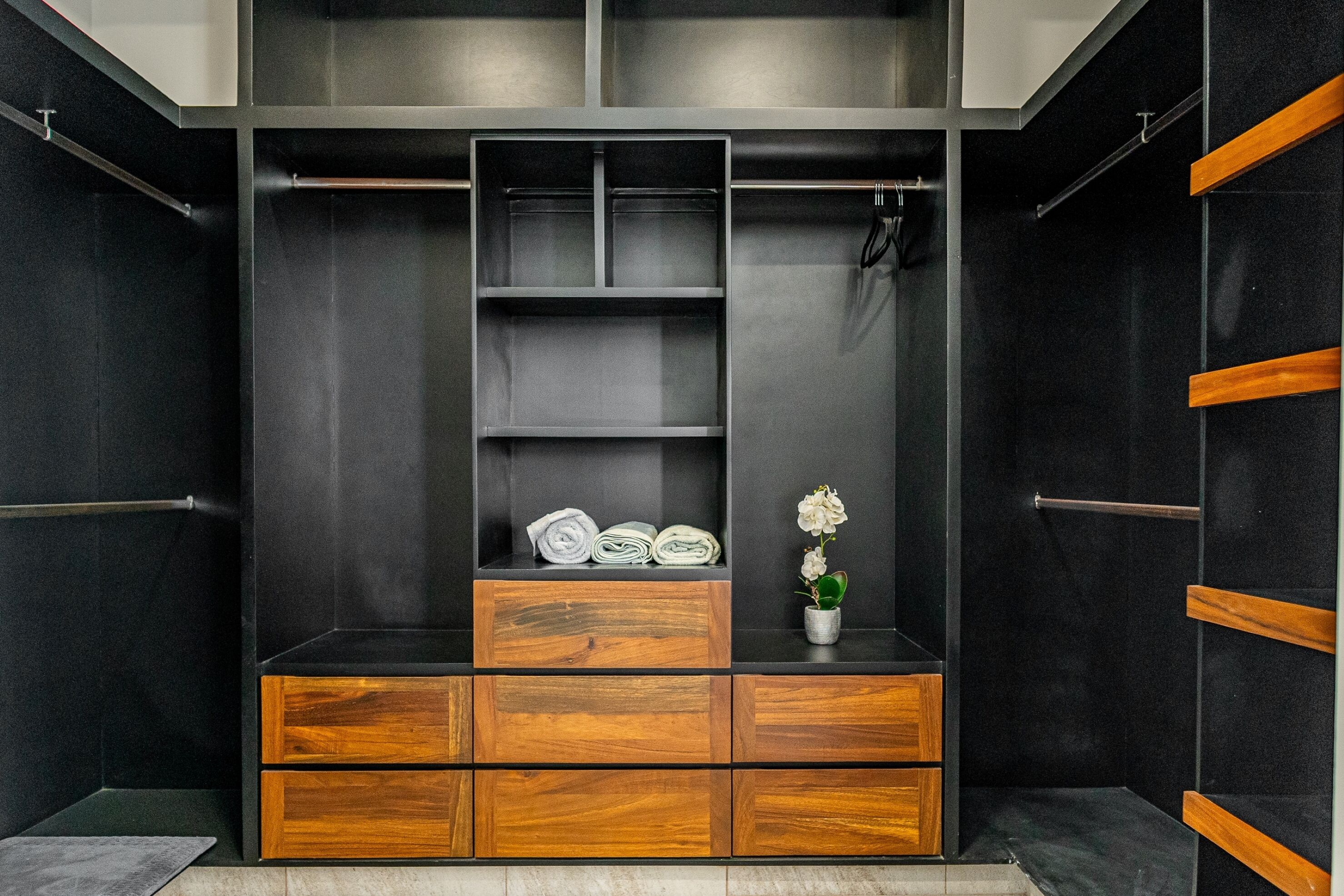 A modern closet with wooden drawers and shelves, a small potted plant, and neatly folded towels.