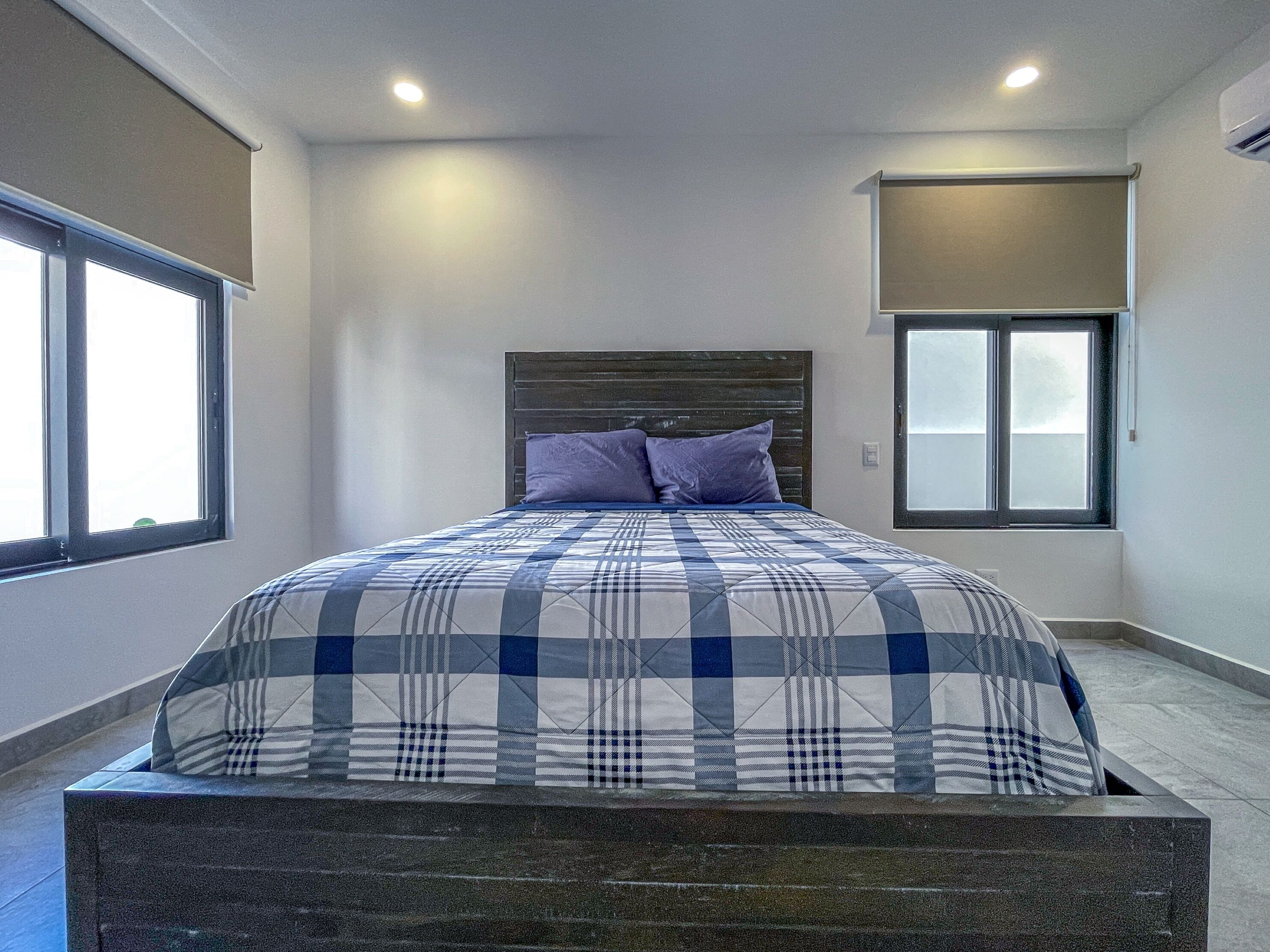 Una camera da letto con un letto, una testata, due finestre e una lampada a soffitto.