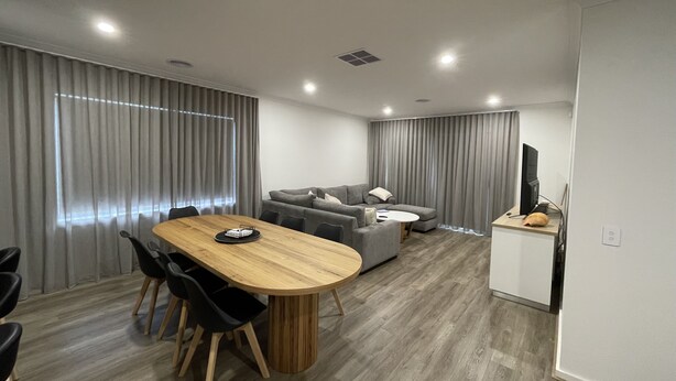 A modern living room with a wooden dining table, grey sofas, and a flat-screen TV.