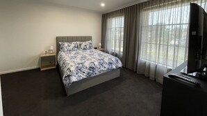 A hotel room with a large bed, a TV, and a window with curtains.