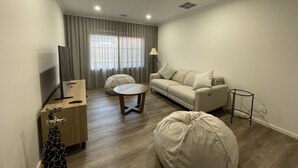 A modern living room with a sofa, a coffee table, a bean bag, a TV stand, and a lamp.