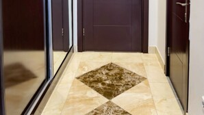 A hallway with a dark brown door, a glass door on the left, and a tiled floor with a diamond pattern. - VIP Room 2 - Ussat Hotel (Ashgabat)