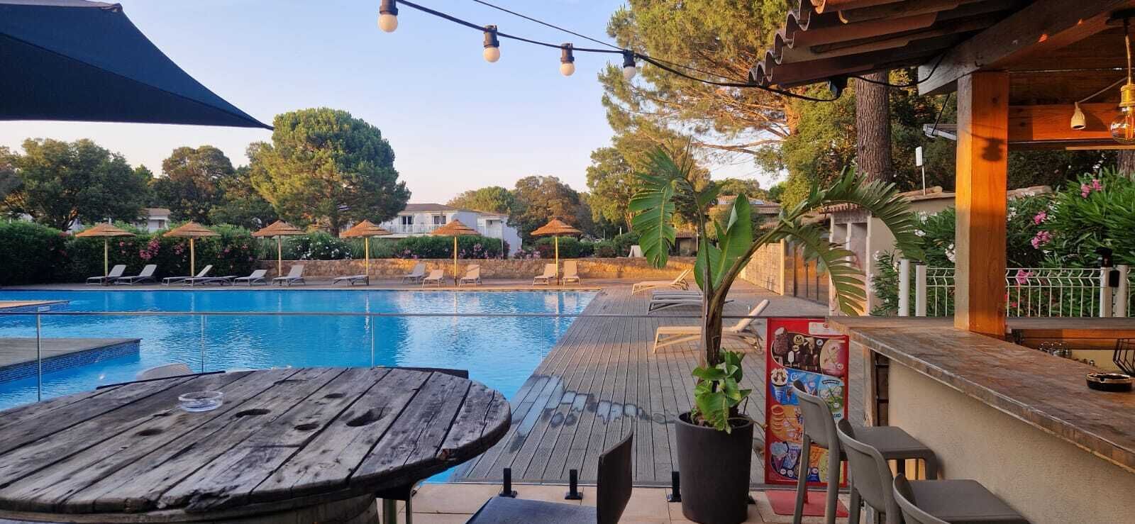 Ein Poolbereich mit Liegestühlen, einem Holztisch und einer Bar mit einer Speisekarte.