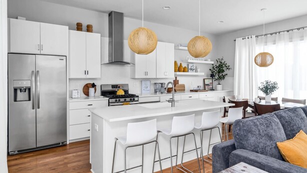 A modern kitchen with white cabinetry, stainless steel appliances, a central island with bar stools, and pendant lighting.