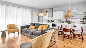 A modern kitchen with white cabinets, a stainless steel refrigerator, and a dining area with wooden chairs and a round table.