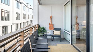 A balcony with outdoor seating, a guitar, and a view of neighboring buildings.