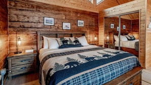 A wooden cabin bedroom with a large bed, a nightstand, a dresser, and a skylight. - Lakeshore Lodging Cabins (Homer)