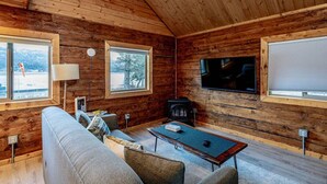 A log cabin interior with a sofa, a coffee table, a fireplace, and a television. - Lakeshore Lodging Cabins (Homer)