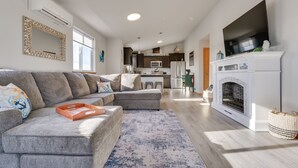 Ein modernes Wohnzimmer mit einem grauen Ecksofa, einem Kamin und einer Küche im Hintergrund.