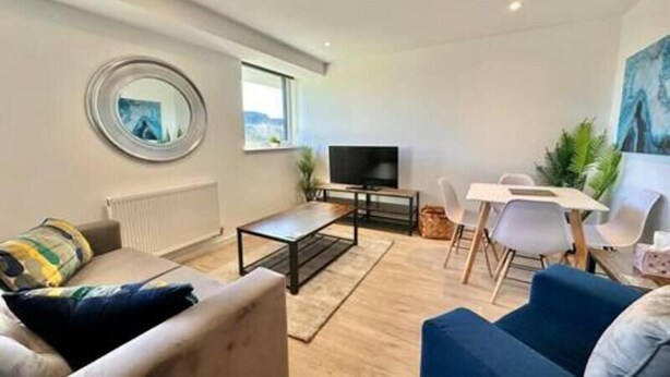 Een moderne woonkamer met een bank, een salontafel, een televisie en een eethoek met stoelen.