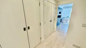 Un couloir avec des portes blanches, un coin cuisine visible au fond, et un plancher de couleur claire.