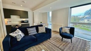 Un salon moderne avec un canapé bleu foncé, un fauteuil assorti et une grande fenêtre donnant sur l’extérieur.