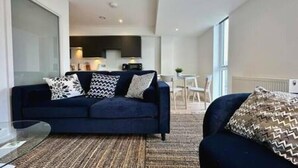 Un salon moderne avec un canapé bleu foncé, des coussins à motifs et un tapis tissé. Une table basse en verre se trouve devant le canapé.