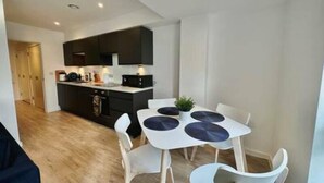 Une cuisine moderne avec des meubles de couleur sombre, un plan de travail blanc et un coin repas comprenant une table et des chaises blanches.