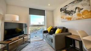 A modern living room with a flat-screen TV, a sofa with yellow cushions, a painting on the wall, and a large window offering a view. - Coates House by Guestz (Bristol)