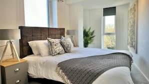 A bedroom with a large bed, two bedside tables, a nightstand, and a window. - Coates House by Guestz (Bristol)