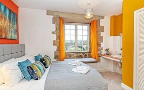 A bedroom with a bed, pillows, a window with curtains, a bathroom with a sink, and a painting on the wall. - Bridge End Mill by Guestz (Settle)