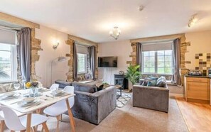 A modern living room with a dining area, grey sofas, a flat-screen TV, and a kitchen with wooden cabinets. - Bridge End Mill by Guestz (Settle)