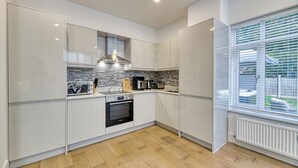A modern kitchen with white cabinetry, a built-in oven, and a stone backsplash. - Eden Grove 2 Bed Holiday Retreat With Hottub (Bolton)
