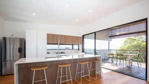 A modern kitchen with a central island, bar stools, and a view of a balcony with outdoor seating.