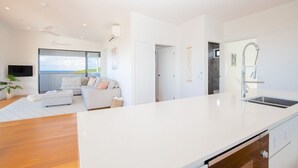 A modern kitchen with a large island, a dining area with a white table and chairs, and a living room with a sofa and a TV.