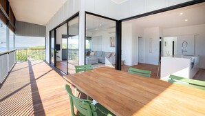A modern interior with a wooden dining table, green chairs, a sofa, and a kitchen area.