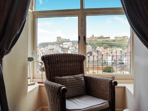 Une chaise en osier avec un coussin, placée près d’une fenêtre donnant sur un bâtiment historique.