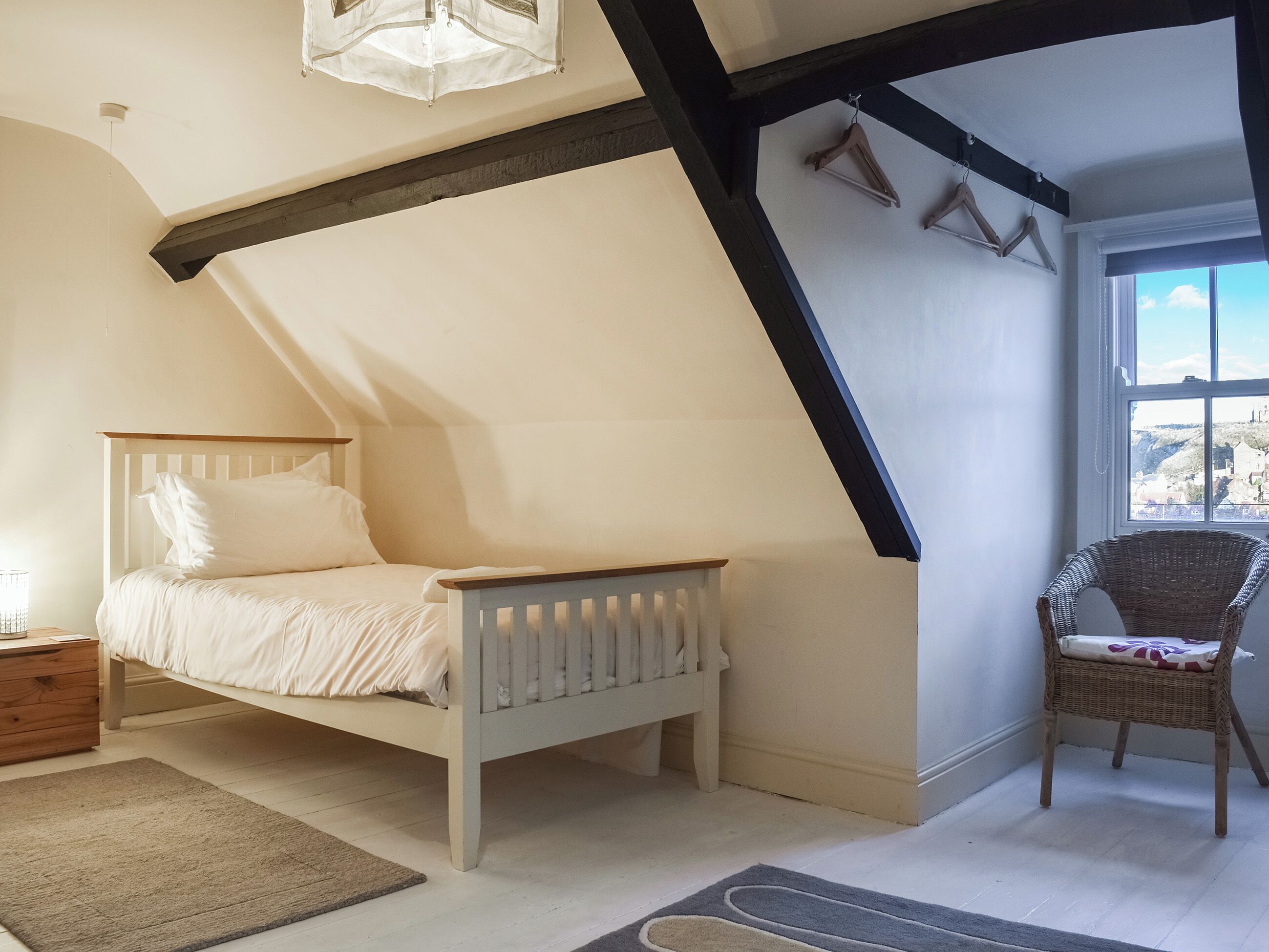 A bedroom with a sloped ceiling, a bed, a chair, and a window with a view.